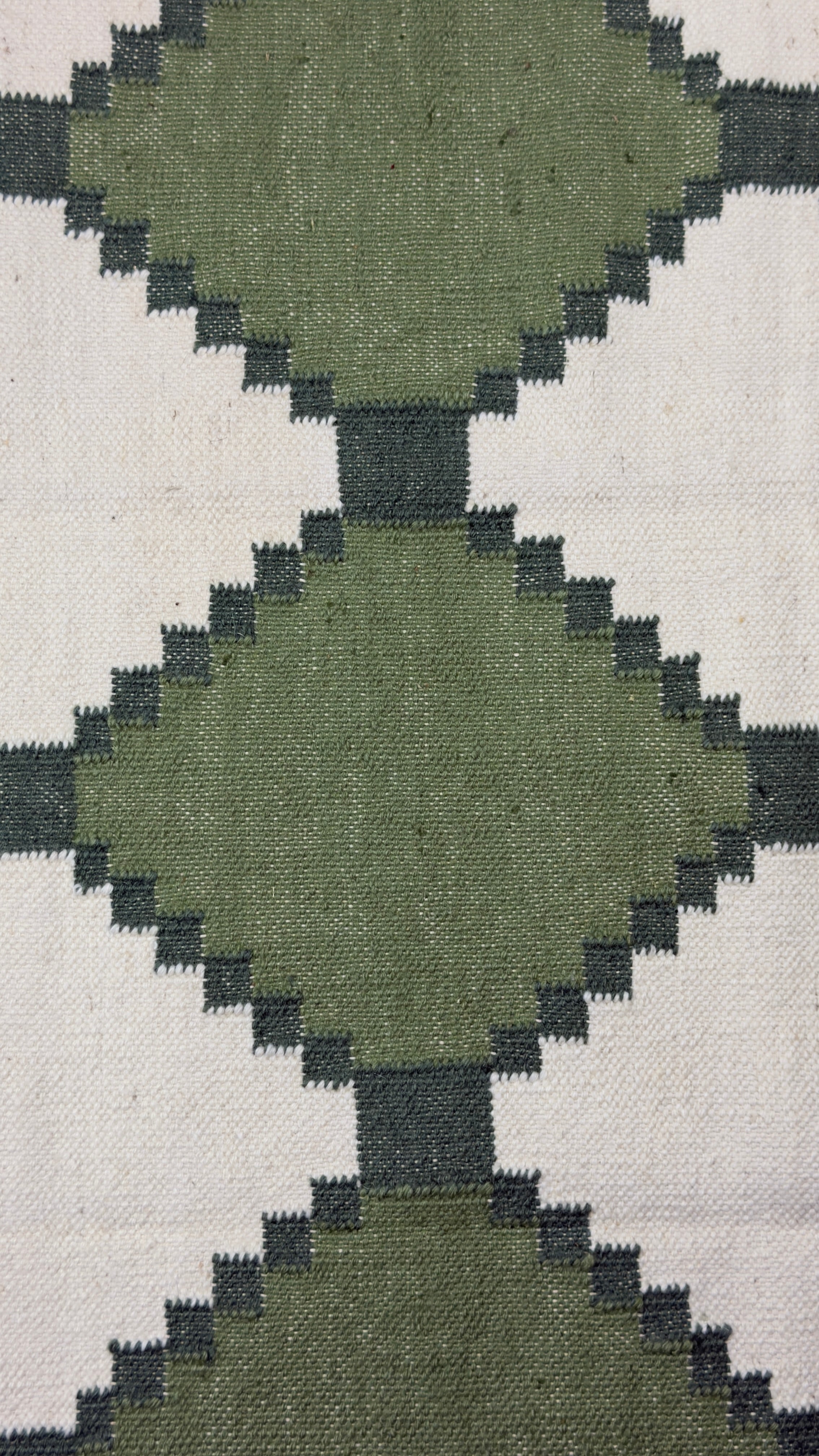 Close-up of a geometric patterned rug with green and beige colors.