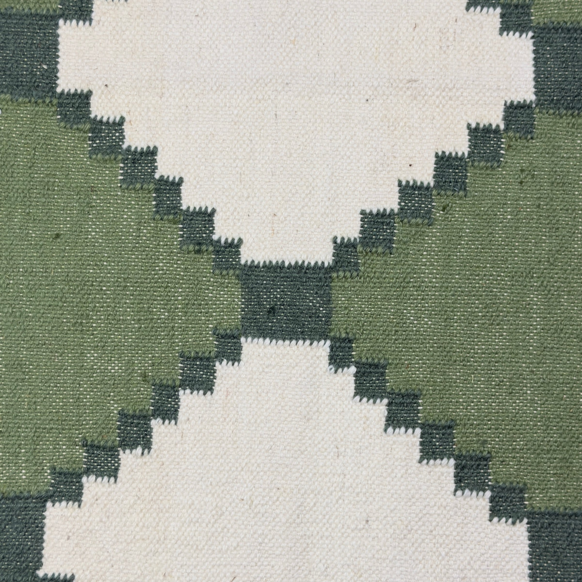Close-up of a geometric patterned rug with green and beige colors.