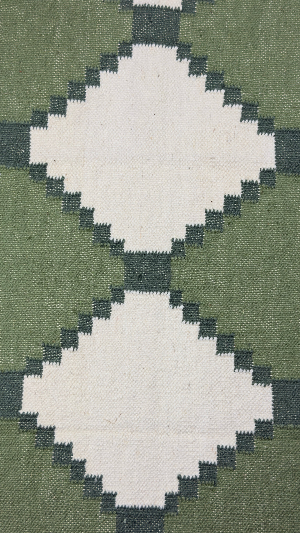 Close-up of a geometric patterned rug with green and beige colors.