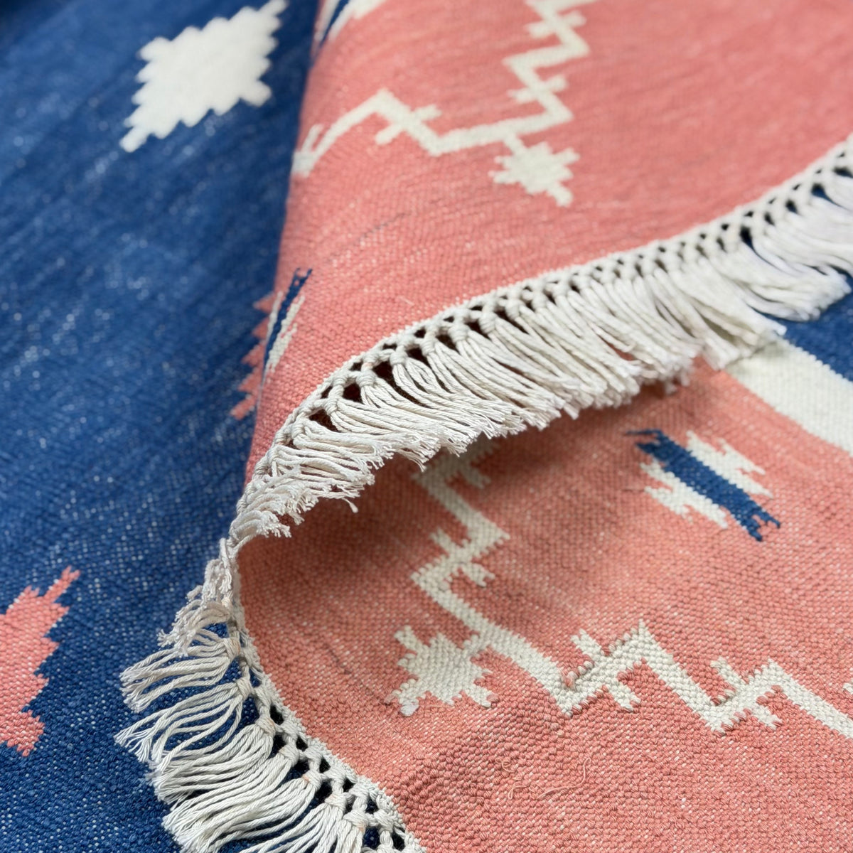 Close-up of a pink and blue patterned rug with white fringe