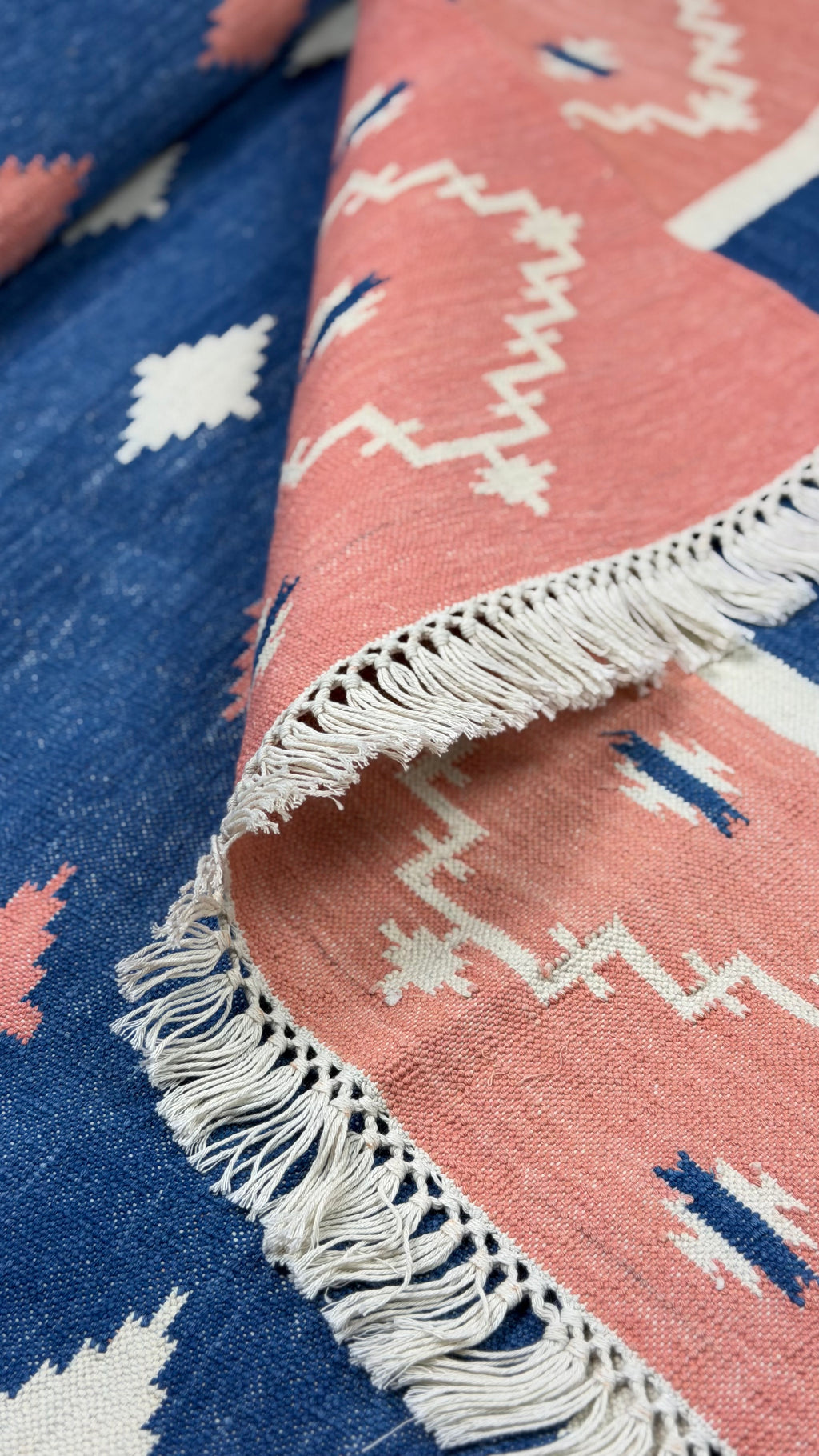 Close-up of a pink and blue patterned rug with white fringe