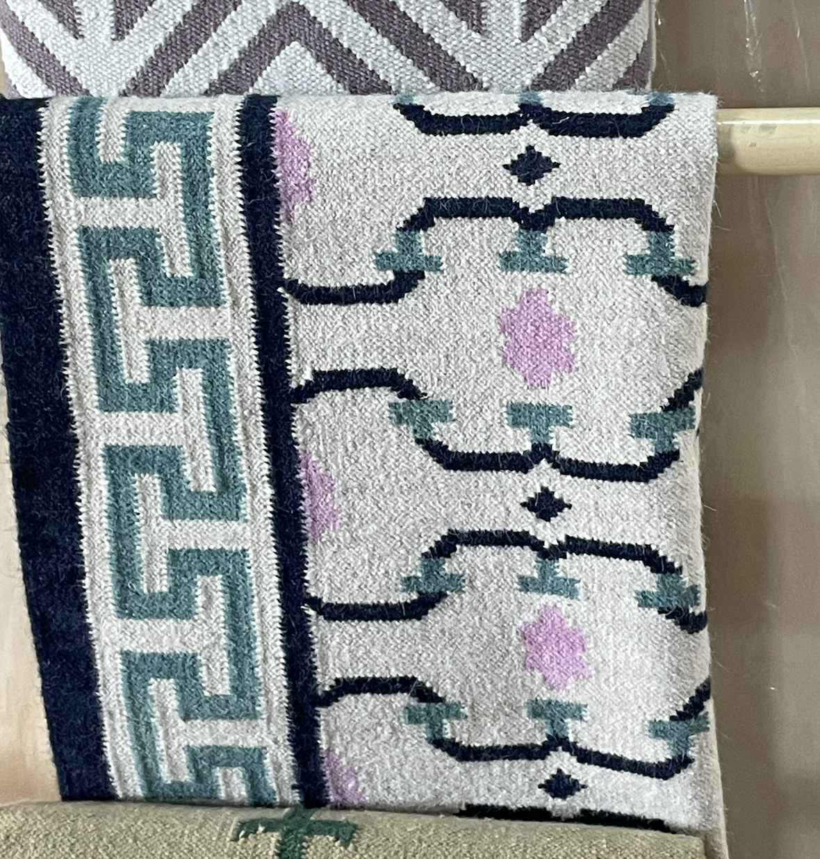 Rug with geometric patterns in shades of blue, pink, and beige on a rack.