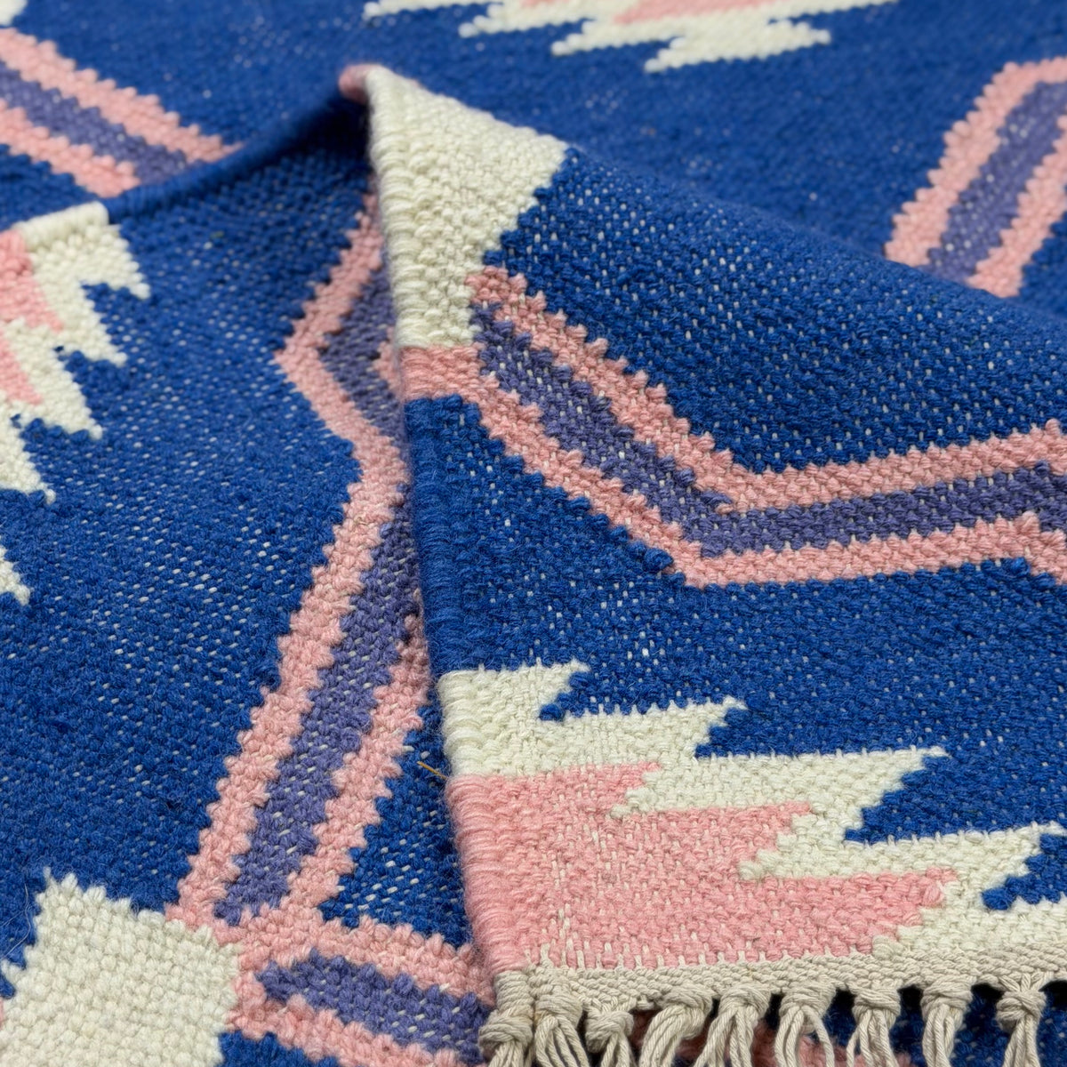 Close-up of a blue and pink patterned rug with tassels.