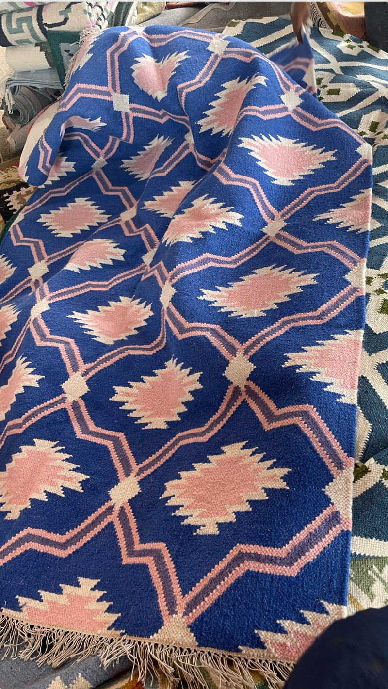 Blue and pink patterned rug with a geometric design on a textured surface.