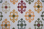 Patterned rug with geometric design in red, orange, green, and beige on a white background